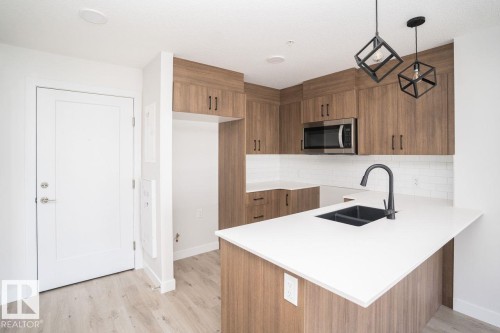 Open kitchen featuring wood-finish cabinetry, white countertops, subway tile backsplash, and stainless steel microwave - #204 2225 44 Av Nw, Edmonton, AB - Indoor Photo Showing Kitchen With Double Sink