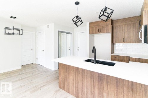 Modern kitchen island featuring a white countertop, integrated black sink, and matte black faucet - #204 2225 44 Av Nw, Edmonton, AB - Indoor Photo Showing Kitchen With Double Sink