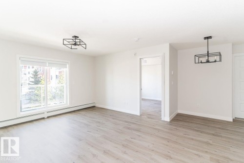 Spacious room featuring wood-finish flooring, white walls, and a large window - #204 2225 44 Av Nw, Edmonton, AB - Indoor Photo Showing Other Room
