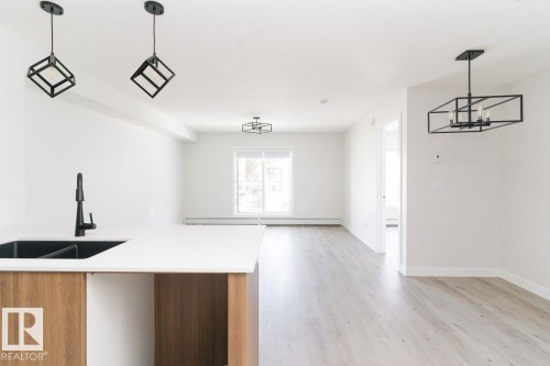 Open-concept living space featuring wood-finish flooring, white walls, and contemporary black light fixtures - #204 2225 44 Av Nw, Edmonton, AB - Indoor
