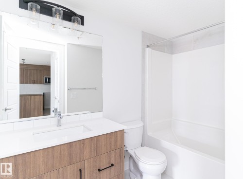Contemporary vanity featuring wood-finish cabinetry, a white countertop, and an integrated rectangular sink with a single-handle faucet - #204 2225 44 Av Nw, Edmonton, AB - Indoor Photo Showing Bathroom