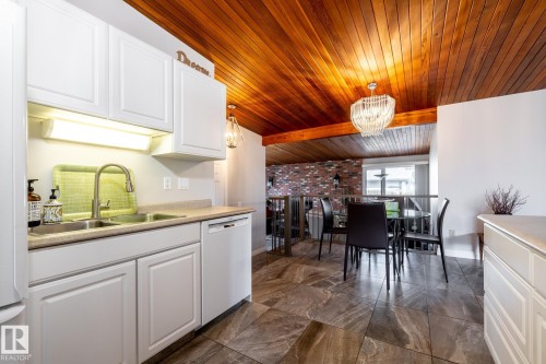 Kitchen area featuring white cabinetry, a double basin stainless steel sink with a gooseneck faucet, light-toned countertops, and a white dishwasher - 16536 103 Street, Edmonton, AB - Indoor Photo Showing Other Room