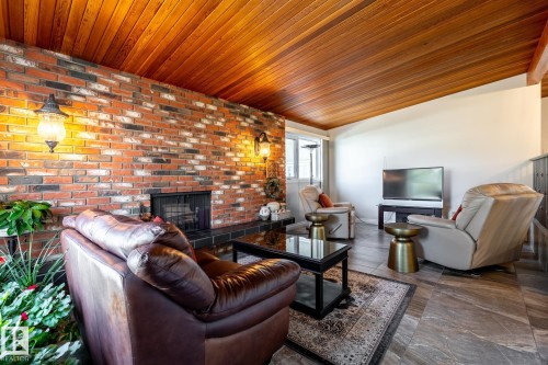 Exposed brick wall featuring a built-in fireplace, wood-plank ceiling, wall sconce lighting, and slate-finish flooring - 16536 103 Street, Edmonton, AB - Indoor Photo Showing Living Room With Fireplace
