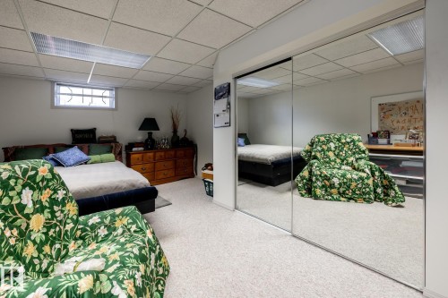 Carpeted room featuring a drop ceiling with integrated lighting, a small window with security bars, and a full wall of mirrored sliding closet doors - 16536 103 Street, Edmonton, AB - Indoor