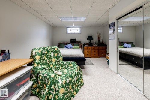 Spacious room featuring light-colored carpeting, a drop ceiling with integrated lighting, and a mirrored closet door - 16536 103 Street, Edmonton, AB - Indoor