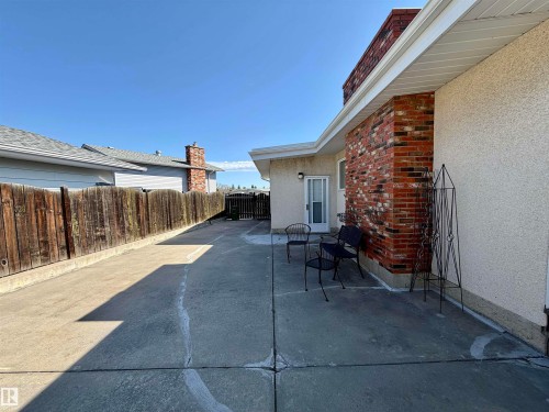 Concrete patio area featuring a textured stucco exterior with brick accents and a secure wooden fence - 16536 103 Street, Edmonton, AB - Outdoor With Exterior