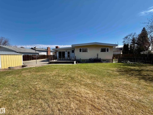 Expansive green space featuring a wood-decked patio, a detached storage shed, a paved driveway, and a privacy fence - 16536 103 Street, Edmonton, AB - Outdoor With Deck Patio Veranda