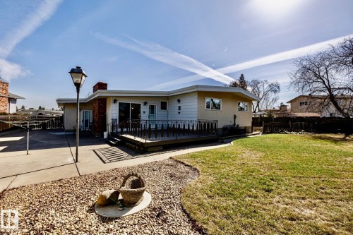 Spacious rear exterior featuring a raised wood-finish deck with dark railings, a concrete patio, and a grass lawn - 16536 103 Street, Edmonton, AB - Outdoor With Deck Patio Veranda