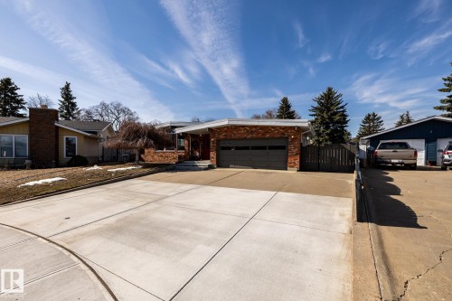 Brick exterior with a dark grey garage door, a concrete driveway, and mature evergreen trees - 16536 103 Street, Edmonton, AB - Outdoor