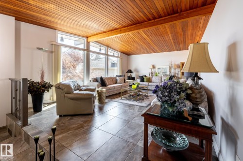 Vaulted wood-paneled ceiling with exposed beam, expansive windows, large format tile flooring, and a contemporary metal railing - 16536 103 Street, Edmonton, AB - Indoor Photo Showing Living Room