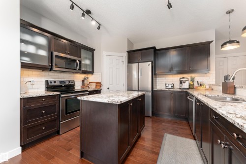 Kitchen featuring dark wood cabinetry, stainless steel appliances, a center island, granite-style countertops, and subway tile backsplash - 22064 95 Avenue, Edmonton, AB - Indoor Photo Showing Kitchen With Double Sink With Upgraded Kitchen