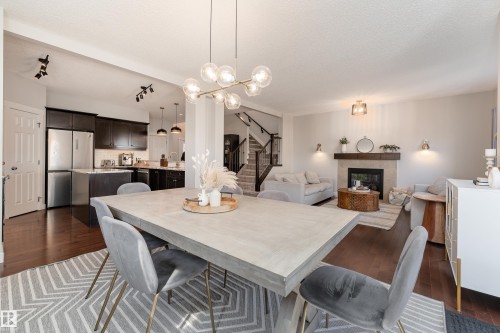 Open-concept dining area featuring a modern chandelier, dark wood-finish flooring, and a patterned area rug - 22064 95 Avenue, Edmonton, AB - Indoor Photo Showing Dining Room With Fireplace