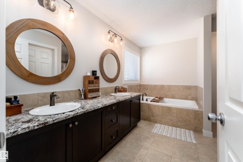 Dual vanity with oval undermount sinks set in a stone-finish countertop, dark wood-finish cabinetry, and individual round framed mirrors - 22064 95 Avenue, Edmonton, AB - Indoor Photo Showing Bathroom