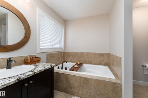 Bathroom featuring a built-in soaking tub with surrounding tile, a vanity with a granite countertop and undermount sink, and a framed oval mirror - 22064 95 Avenue, Edmonton, AB - Indoor Photo Showing Bathroom