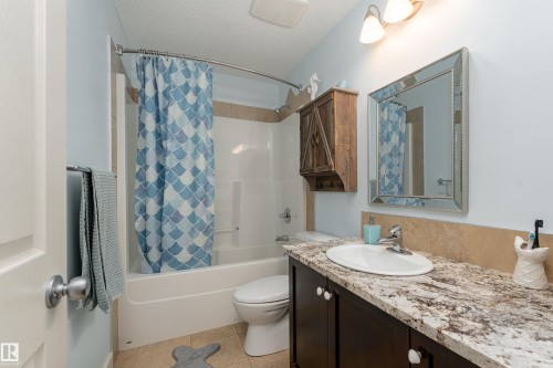 Bathroom featuring a single vanity with stone-finish countertop, undermount sink, and dark wood cabinetry - 22064 95 Avenue, Edmonton, AB - Indoor Photo Showing Bathroom