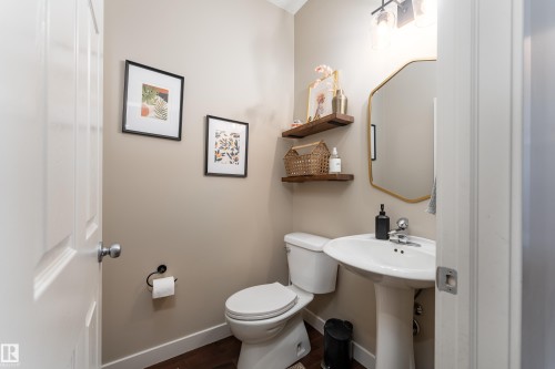 Powder room featuring a pedestal sink, gold-framed mirror, two floating wood shelves, and wood-finish flooring - 22064 95 Avenue, Edmonton, AB - Indoor Photo Showing Bathroom