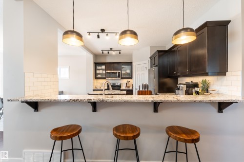 Kitchen featuring a breakfast bar with stone-finish countertop, dark wood-finish cabinetry, and white subway tile backsplash - 22064 95 Avenue, Edmonton, AB - Indoor Photo Showing Kitchen