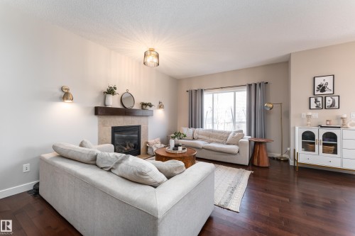 Spacious living area featuring rich wood-finish flooring, a tiled fireplace with a wood mantle, and a large window providing ambient light - 22064 95 Avenue, Edmonton, AB - Indoor Photo Showing Living Room With Fireplace