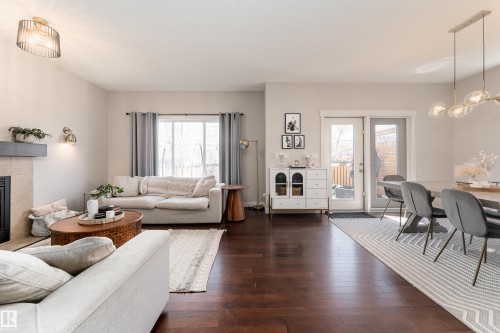 Open-concept living space featuring wood-finish flooring, a fireplace with a stone surround and wood mantel, and expansive windows - 22064 95 Avenue, Edmonton, AB - Indoor Photo Showing Living Room With Fireplace