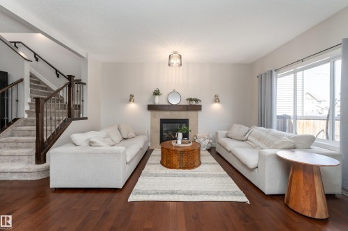 Living area featuring wood-finish flooring, a fireplace with a tile surround and wood mantel, and large windows with privacy blinds - 22064 95 Avenue, Edmonton, AB - Indoor Photo Showing Living Room With Fireplace