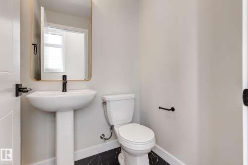 Powder room featuring a white pedestal sink with a matte black faucet, a gold-framed mirror, and dark tile flooring - 44 16231 19 Avenue, Edmonton, AB - Indoor Photo Showing Bathroom