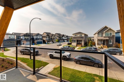 Balcony with glass railing and wood-tone support beams overlooking a residential street with contemporary homes - 44 16231 19 Avenue, Edmonton, AB - Outdoor With Balcony