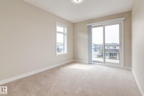Bright interior space featuring a large sliding glass door, a window with white trim, light neutral wall paint, and beige carpet flooring - 44 16231 19 Avenue, Edmonton, AB - Indoor Photo Showing Other Room
