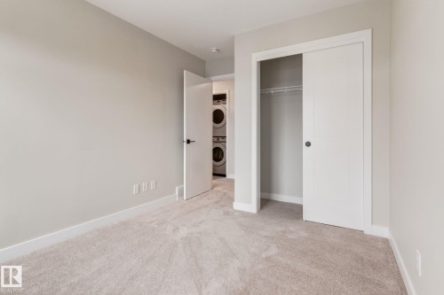 Carpeted room featuring a closet with bi-fold doors and an adjacent laundry area with a stacked washer and dryer - 44 16231 19 Avenue, Edmonton, AB - Indoor Photo Showing Other Room