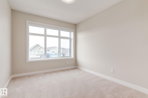 Neutral-toned room featuring a large multi-pane window with white trim, light beige wall paint, and coordinating carpeting - 44 16231 19 Avenue, Edmonton, AB - Indoor Photo Showing Other Room