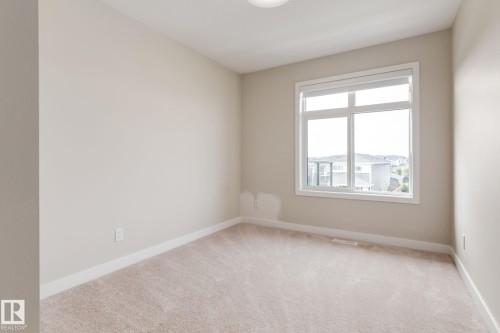 Neutral-toned room featuring a large window, light beige carpeting, white baseboards, and a flush mount ceiling light - 44 16231 19 Avenue, Edmonton, AB - Indoor Photo Showing Other Room