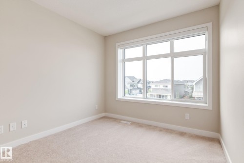 Bedroom with a large multi-pane window, neutral-toned carpet, light-colored wall paint, white baseboards, and white window trim - 44 16231 19 Avenue, Edmonton, AB - Indoor Photo Showing Other Room