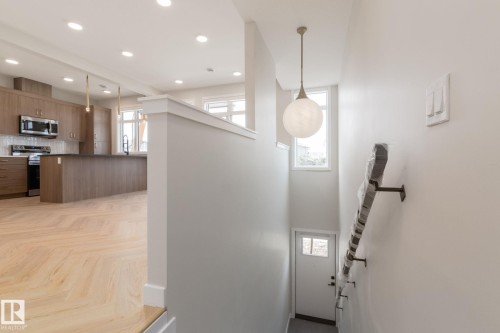 Modern kitchen featuring wood-finish cabinetry, stainless steel appliances, a large island with a dark countertop, and recessed lighting - 44 16231 19 Avenue, Edmonton, AB - Indoor Photo Showing Kitchen With Upgraded Kitchen