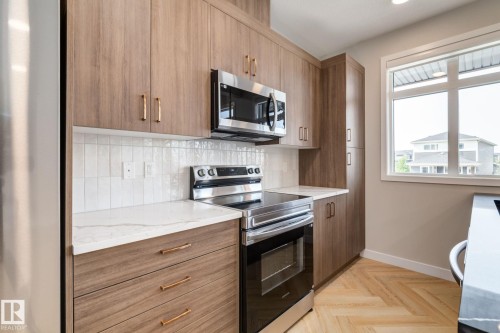 Contemporary kitchen featuring wood-finish cabinetry with golden hardware, white subway tile backsplash, and light-toned countertops - 44 16231 19 Avenue, Edmonton, AB - Indoor Photo Showing Kitchen