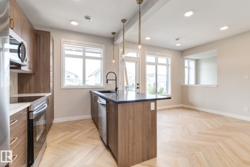 Open-concept kitchen featuring wood-finish cabinetry, stainless steel appliances, a center island with a dark countertop and undermount sink, and herringbone wood-finish flooring - 44 16231 19 Avenue, Edmonton, AB - Indoor Photo Showing Kitchen With Upgraded Kitchen