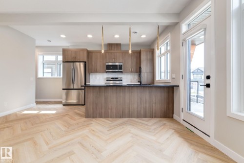 Open-concept kitchen featuring wood-finish cabinetry, stainless steel appliances, a dark countertop island, and pendant lighting - 44 16231 19 Avenue, Edmonton, AB - Indoor Photo Showing Kitchen