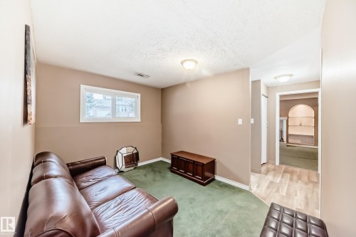 This versatile living area features a window, providing natural light, and a mix of green carpeting and light-toned flooring - 9813 152 Street, Edmonton, AB - Indoor