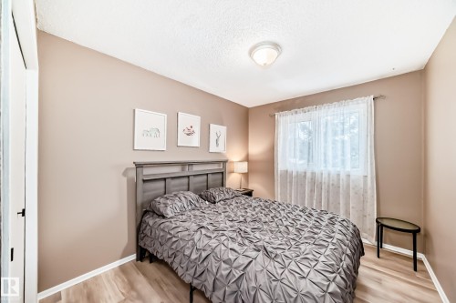 This bedroom features light wood-look flooring, neutral-toned walls, and a window with sheer curtains - 9813 152 Street, Edmonton, AB - Indoor Photo Showing Bedroom