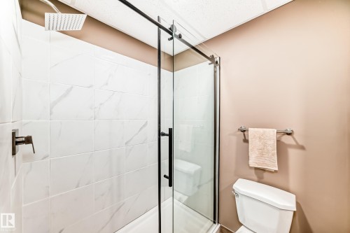 The bathroom features a shower with white tiled walls and a rain shower head, enclosed by a clear glass door with black framing - 9813 152 Street, Edmonton, AB - Indoor Photo Showing Bathroom