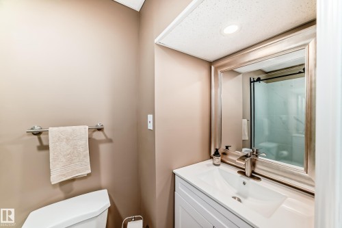 The bathroom features a modern vanity with a white countertop and an integrated sink, complemented by a framed mirror - 9813 152 Street, Edmonton, AB - Indoor Photo Showing Bathroom