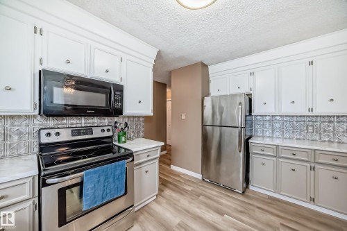 The kitchen features white upper cabinetry, grey lower cabinetry, and stainless steel appliances - 9813 152 Street, Edmonton, AB - Indoor Photo Showing Kitchen