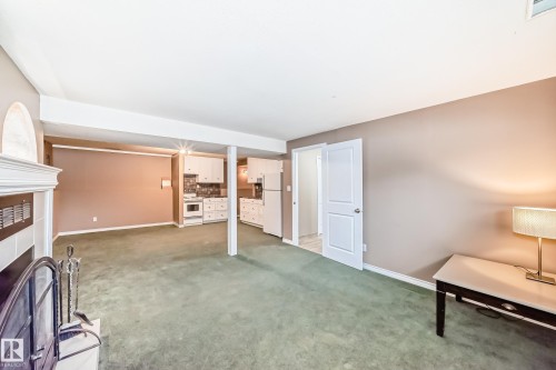 Living area featuring green carpeting, neutral-toned walls, and a white fireplace with a decorative arch - 9813 152 Street, Edmonton, AB - Indoor