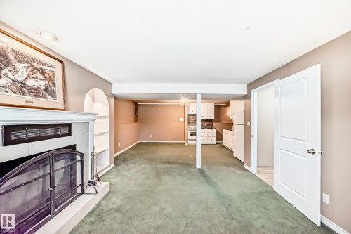 Living area featuring green carpet flooring, a white fireplace with a dark screen, and an arched built-in shelving unit - 9813 152 Street, Edmonton, AB - Indoor Photo Showing Other Room With Fireplace