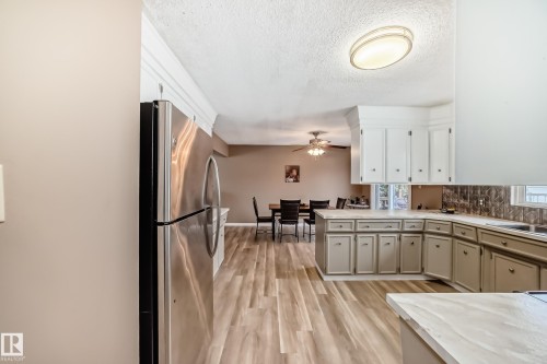 Kitchen featuring wood-style flooring, white upper cabinetry, and a stainless steel refrigerator - 9813 152 Street, Edmonton, AB - Indoor Photo Showing Kitchen