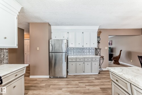 The kitchen features wood-look flooring, light-colored cabinetry, a stainless steel refrigerator, and marbled countertops - 9813 152 Street, Edmonton, AB - Indoor Photo Showing Kitchen