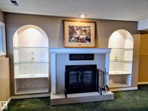 Living room featuring a fireplace with a tiled surround, a white mantel, and an arched fire screen - 9813 152 Street, Edmonton, AB - Indoor With Fireplace