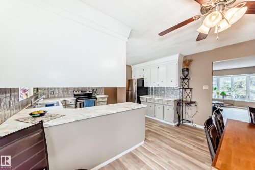The kitchen features light-colored countertops, white cabinetry, a stainless steel refrigerator, and a dark-colored stove with a matching backsplash - 9813 152 Street, Edmonton, AB - Indoor