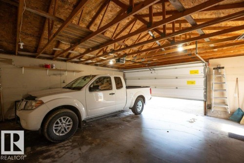 Garage space featuring an exposed wood-beam ceiling, concrete flooring, overhead lighting, an automatic garage door opener, and a white paneled garage door - 10812 109 Street, Westlock, AB - Indoor Photo Showing Garage