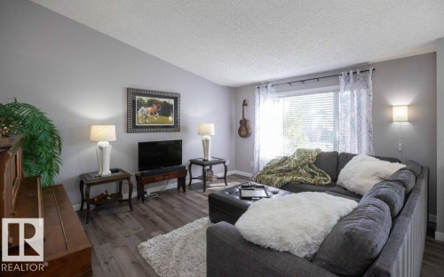 Living area featuring wood-finish flooring, a large window with blinds, and a built-in wall sconce - 10812 109 Street, Westlock, AB - Indoor Photo Showing Living Room