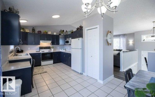 Kitchen featuring dark cabinetry, white appliances, solid surface countertops, and tiled flooring - 10812 109 Street, Westlock, AB - Indoor Photo Showing Kitchen