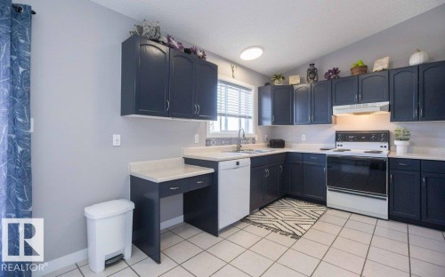 Kitchen featuring dark cabinetry, light countertops, an electric range, and a built-in dishwasher - 10812 109 Street, Westlock, AB - Indoor Photo Showing Kitchen